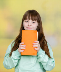 Happy teen girl with Downs syndrom holds a book at summer park
