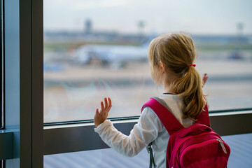 Fototapeta na wymiar Little Girl at the Airport Waiting for Boarding at the Big Window. Cute Kid Stands at the Window against the Backdrop of Airplanes. Looking Forward to Leaving for a Family Summer Vacation