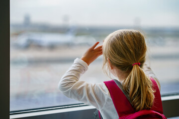 Little Girl at the Airport Waiting for Boarding at the Big Window. Cute Kid Stands at the Window against the Backdrop of Airplanes. Looking Forward to Leaving for a Family Summer Vacation