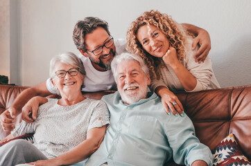 Happy bonding family group relaxing on sofa at home having fun and laughing. Handsome people, parents and adult sons, two generations looking at camera