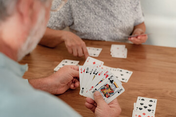 Closeup on senior couple at home in competition playing with cards on a wooden table. Retirement...