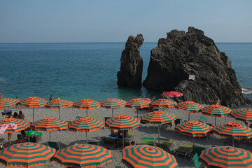 Cinque Terre, Italy - tourists relax under colorful beach parasols in Monterosso al Mare, a seaside village on the rugged Italian Riviera coast. Summer travel vacation background.