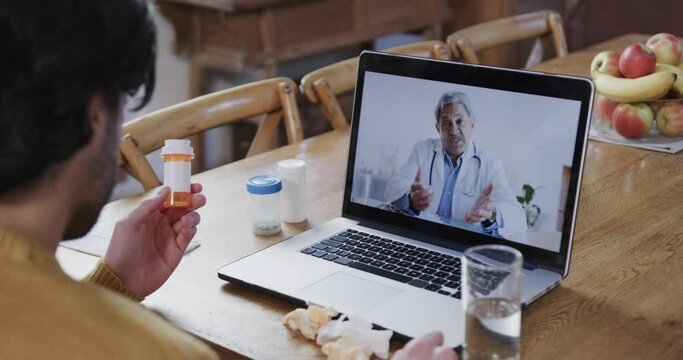 Caucasian man holding medication making video call using laptop with male doctor, slow motion