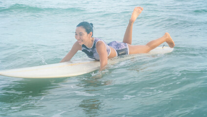 Asian women wearing swimsuits hobby happy fun surfing waves on board in the sea is an exciting water sport on the beach in Thailand