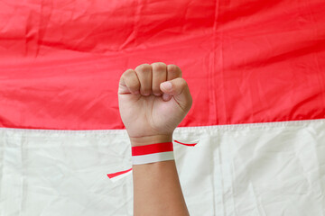Close up of male hand with red and white ribbon raising up in the air fighting to celebrate Indonesia's independence day. Concept of election movement.