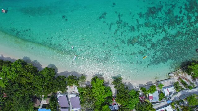 Top Down Aerial View Of Turquoise Blue Beach Shore With Resort Buildings And Lush Green Tree Tops. Hd Drone Shot.
