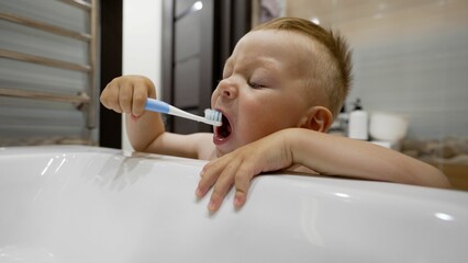 A little boy brushes his teeth in front of the sink. Oral hygiene. Cute baby brushes his teeth in the bathroom. Little boy brushes his teeth.