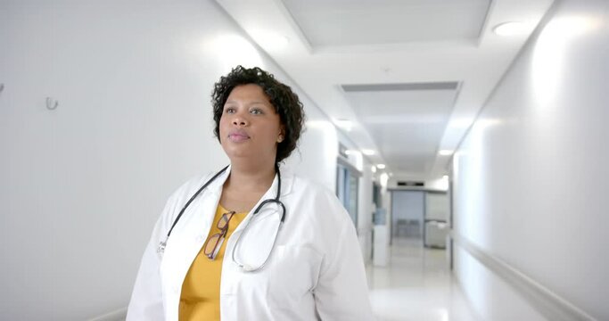 African american female doctor walking in hospital corridor, slow motion