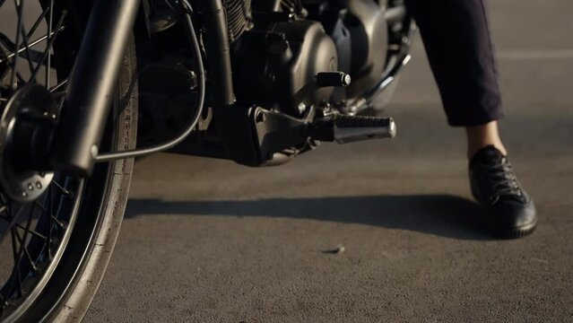 The motorcycle stops and the man's foot puts the parking footrest on the asphalt. Summer riding on bikes. The shadow of the mechanisms on the asphalt. Metal parts.