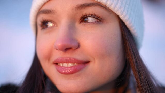 Headshot of young beautiful happy woman in sunrise sunshine looking away smiling. Close-up portrait of relaxed confident Caucasian female tourist enjoying dawn on winter morning outdoors. Slow motion