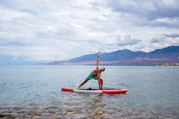 Virabhadrasana. a man does a war pose on a surfboard with a paddle