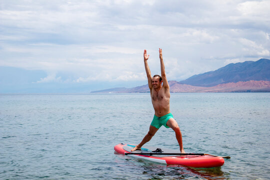 Virabhadrasana. a man does a war pose on a surfboard with a paddle