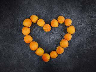 Delicious ripe Fresh juicy apricots on black background, close-up. Selection of healthy vegetarian food, detox or diet concept. View from above apricots lie on table in shape of heart, top studio shot
