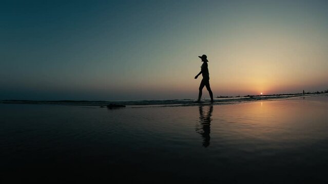 silhouette of a woman walking along the seashore. Spiritual Peace Meditation. A happy girl walks along the seashore against the backdrop of sunset. side view.