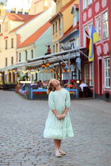 Summer portrait of a girl in a beautiful dress. walking along the beautiful streets of the old city in Riga. Evening lighting, cafes on the streets, flags  Lithuania and Ukraine. Travel,tourism, walks