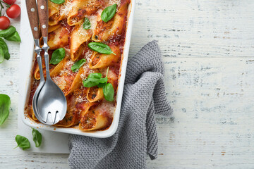 Cannelloni or conchiglioni. Baked stuffed pasta shells with bolognese meat sauce, tomatoes, basil on rustic white wooden table. Traditional Italian bolognese baked pasta with parmesan. Italian cuisine