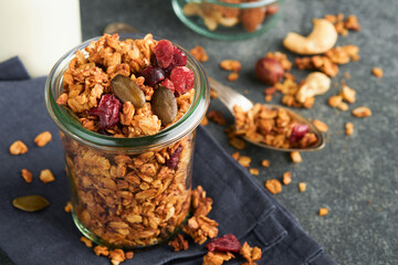 Homemade granola in glass jar with greek yogurt or milk and cashews, almonds, pumpkin with dried cranberry seeds in dark grey table background. Healthy energy breakfast or snack. Top view