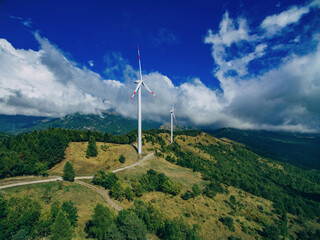 Aerial view of windmills in summer Italy landscape with green hills and blue cloud sky. Wind...
