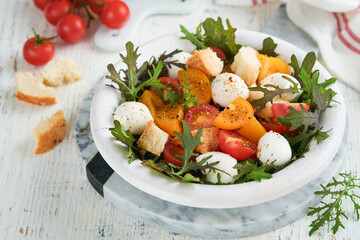 Tuscan Panzanella. Cherry Tomatoes salad with arugula, basil, mozzarella and bread crackers on white bowl. Traditional italian salad. Mediterranean healthy food and cuisine.