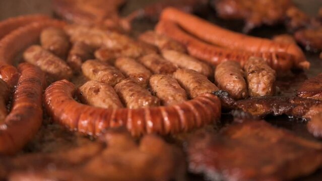 Closeup shot of smoking sausages, cevapi and chuck meat in lard - cooking in slow motion, trucking shot
