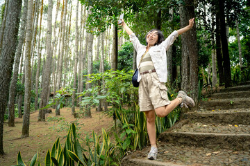 Asian woman holding a mobile phone with a happy expression in the forest