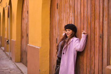 Young woman, beautiful, straight brown hair, sweater, coat and black beret, leaning on a wooden door, happy and carefree. Concept beauty, fashion, autumn, winter, cold.