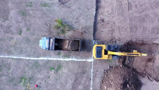 Backhoe moving earth and loading dump truck. Aerial shot with drone  