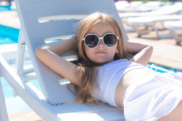 Cute adorable blonde little kid girl enjoy having fun relaxing on sunbed near the pool. Child...