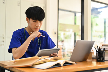 Medical student man wearing blue scrubs using digital tablet, preparing for university exams....