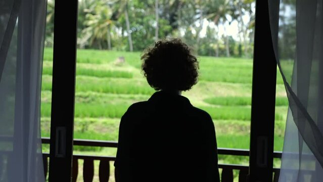 Silhouette of a woman opens the curtains in the morning. Curly blonde opens the curtains on the balcony in a luxury room. The tourist opens the curtains and goes to the terrace to enjoy the sunrise.
