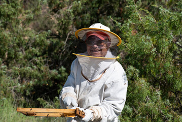 portrait of a man in his eighties in a beekeeping protective suit, smiling and missing a tooth, bee...