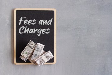 Top view image of money and chalkboard with text FEES AND CHARGES, Business and finance concept