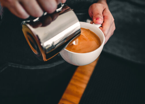 Close-up of the hand of a professional barista in a coffee shop making  pouring steamed milk into the coffee cup making latte menu