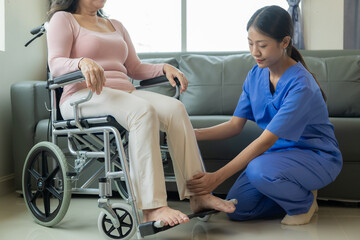 Asian female physiotherapist helping elderly woman stretch hamstrings and doing thigh or leg...