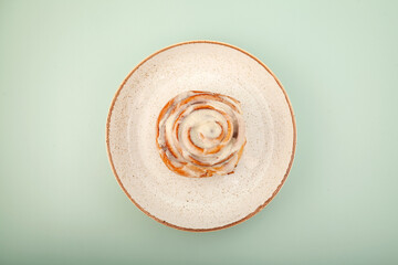 Cinnamon roll or cinnabon in paper box on the plate on green background, top view. Homemade sweet...
