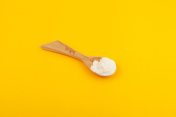 Guar gum powder or guaran in wooden spoo on yellow background, selective focus. Design element. Food additive E412. Thickening agent. Stabilizer and Fat Replacer