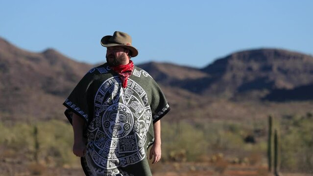 A Desperado man wearing a poncho, red bandanna, and a cowboy hat in the Sonoran Desert. Medium Shot.