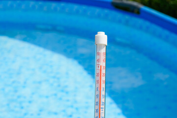 Termometr trzymany w ręce na tle basenu ogrodowego mierzy temperaturę w słońcu  - obrazy, fototapety, plakaty