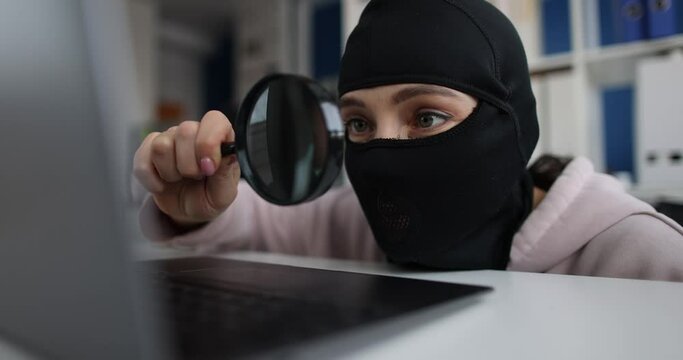 Woman hacker in balaclava near laptop, close-up, shallow focus. Internet fraud, theft of crypto assets