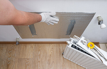 Foil thermal insulation on the wall behind the heating radiator at home. Thermal insulation of the apartment, to save money on utilities, heating. Energy-saving technology. 