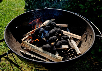 fire up the grill using wood and a lighter. the briquettes will ignite and then it will be possible to throw the meat on the grill. the garden party is about to begin - obrazy, fototapety, plakaty