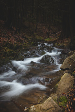 Stream of water rushes through a rocky riverbed in the Beskid forests in autumn weather. Long exposure, flowing water