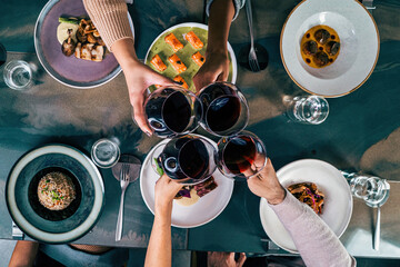 Toast Among Friends in a Fusion Restaurant - Overhead view of four friends making a toast with red wine over a fusion restaurant table with various dishes