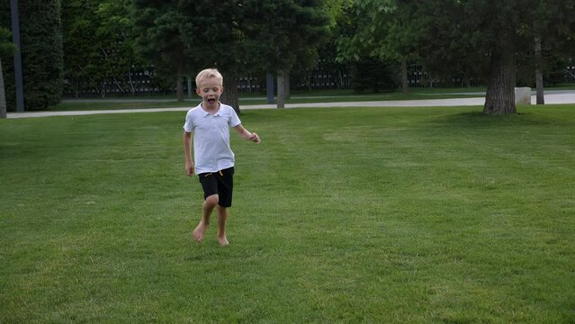 Funny girl and boy running barefoot on the lawn in the park in the evening at sunset, children running and laughing. The boy runs across the grass and falls. Children's fun in the city park in summer.