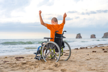 Fototapeta premium A disabled person on his back in a wheelchair on the beach with open arms enjoying the freedom of the sea and nature