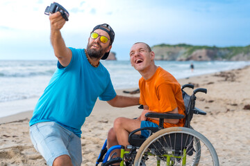 A disabled person in a wheelchair on the beach with a friend taking a selfie