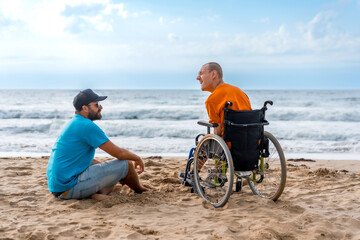 Fototapeta premium Portrait a disabled person in a wheelchair on the beach with a friends sitting looking at the sea