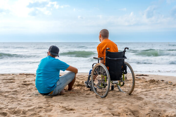 Portrait a disabled person in a wheelchair on the beach with a friends sitting looking at the sea