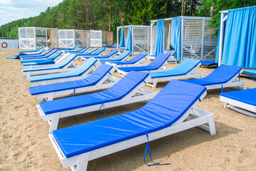 Wooden chaise longue for relaxing on the beach with a soft removable mattress. Relaxing on the beach by the river.  Summer tan by the water. A relaxation area with sun loungers on the sandy beach.