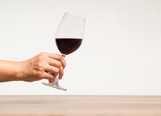Hand holding a glass of red wine against a gray background.